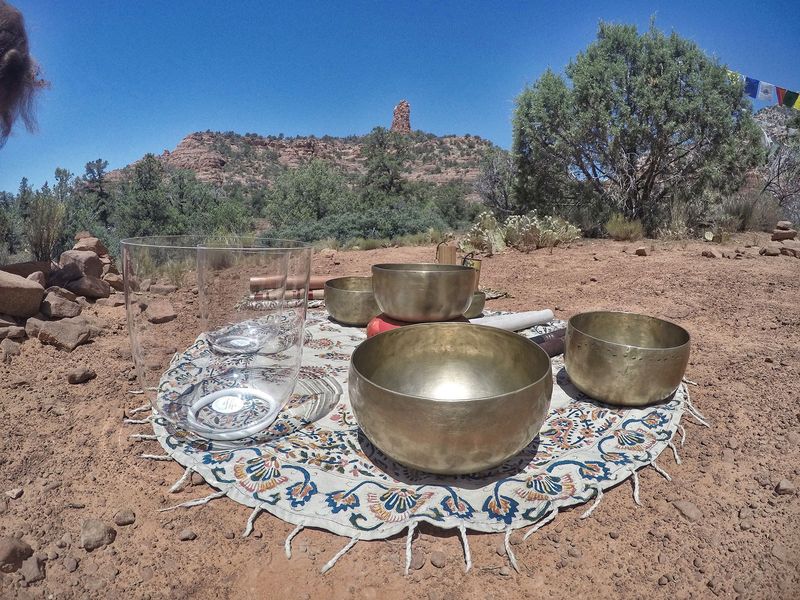 Two clear quartz singing bowls beside hammered brass Himalayan bowls on an embroidered cloth in the red rocks
