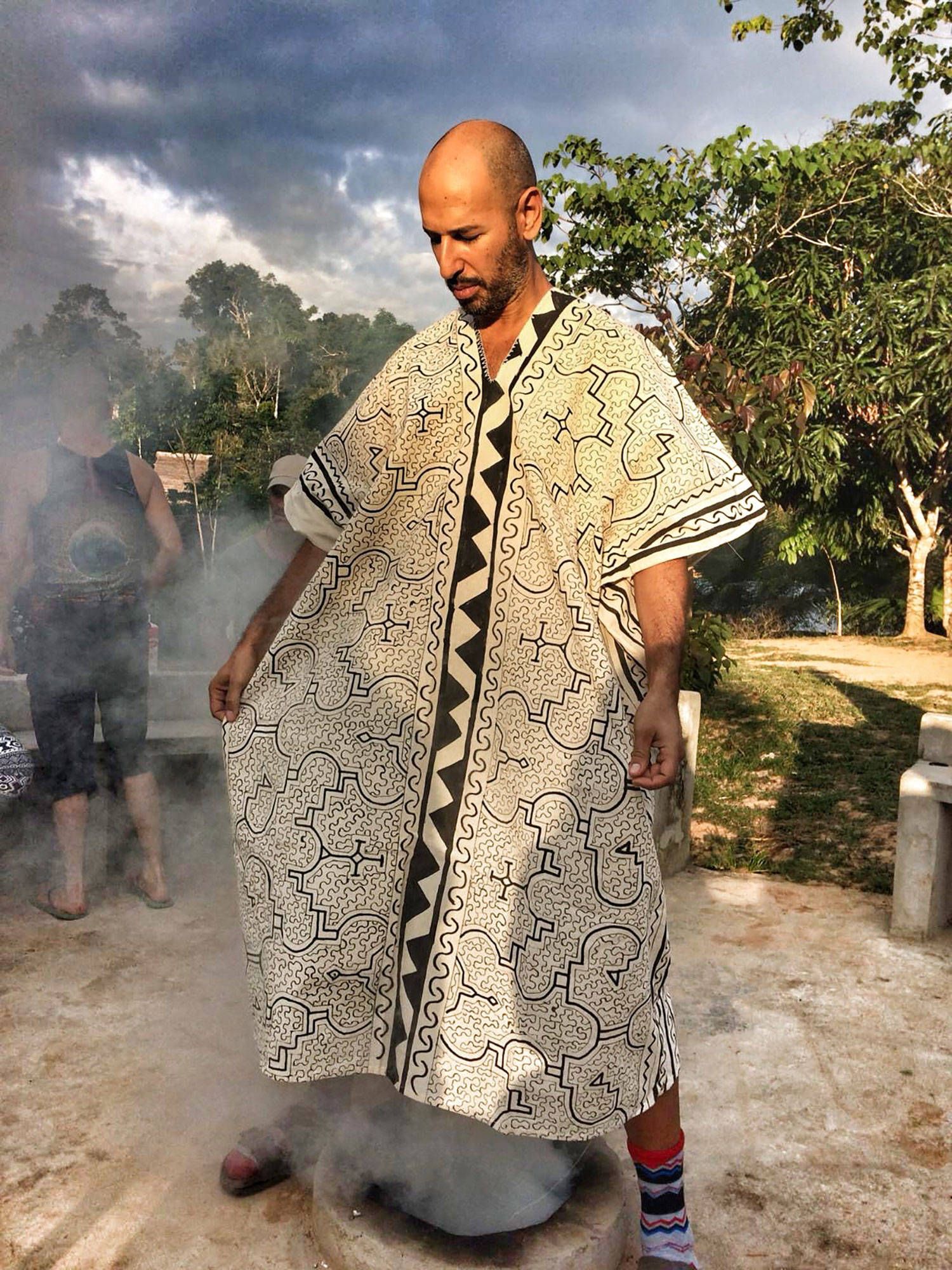 Hamid standing in the smoke of a palo santo bath, wearing a robe printed with Shipibo pattern