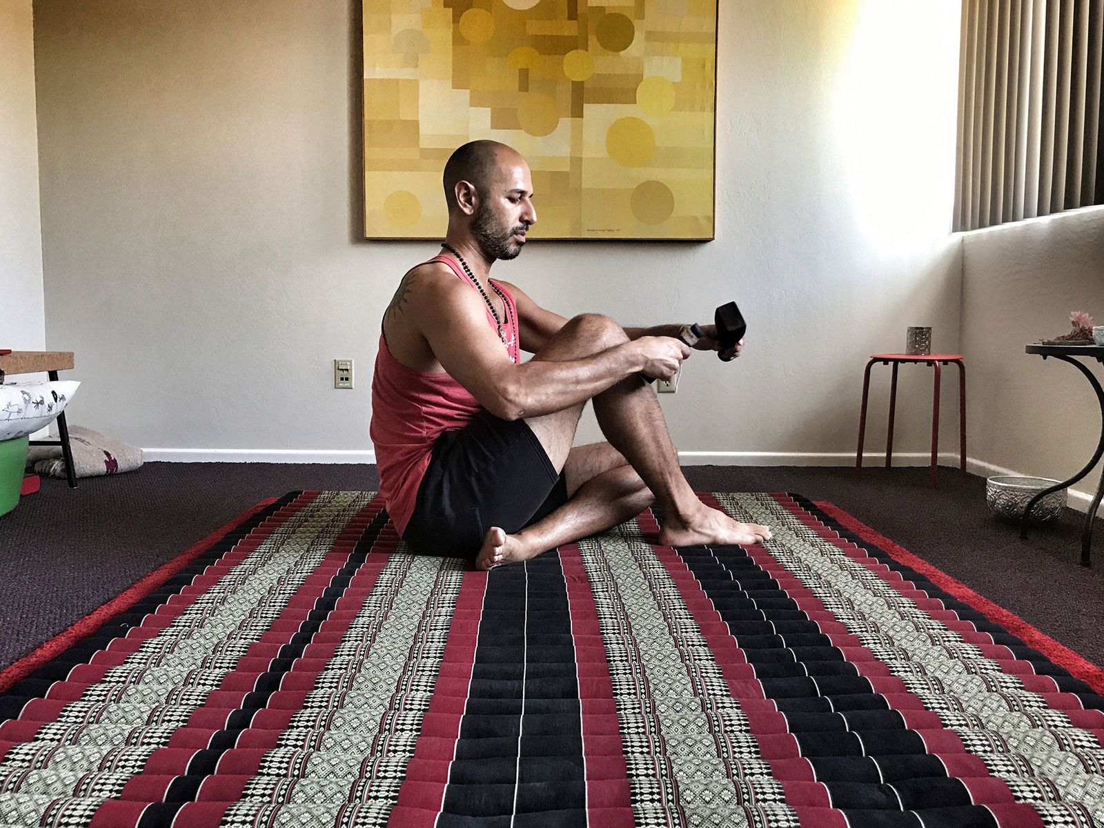 Hamid seated on a striped Thai mat, tapping a wooden peg along his own leg with a Tok Sen mallet