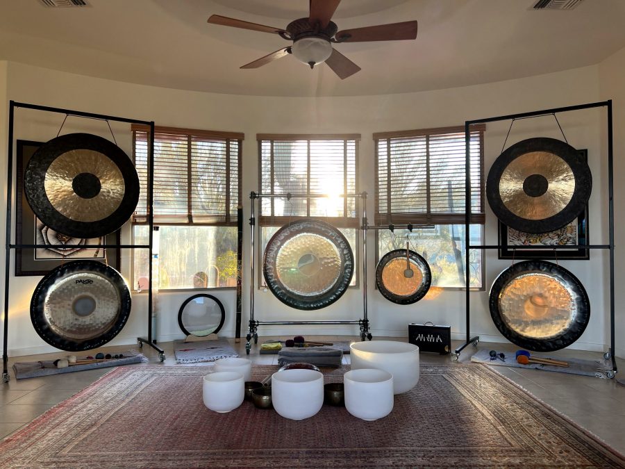 Six gongs hanging on stands around the curved window wall of the room in New River, crystal and Himalayan bowls on a rug in the middle of the floor, morning sun coming through the blinds