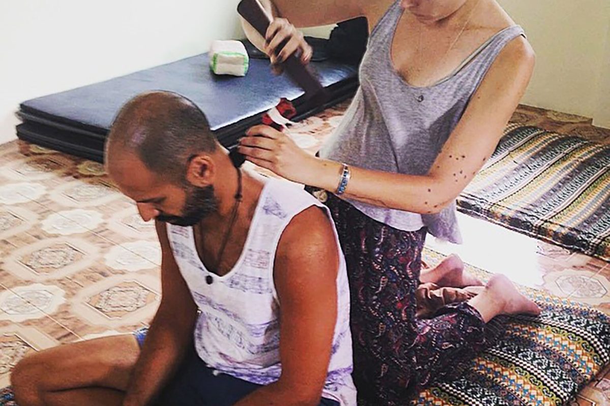 A student practising Tok Sen on Hamid's shoulders as he sits cross legged on a Thai mat