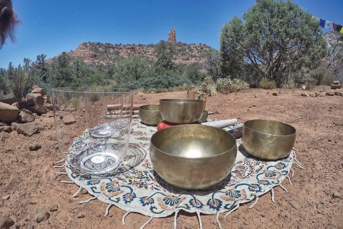 Two clear quartz singing bowls beside hammered brass Himalayan bowls on an embroidered cloth in the red rocks
