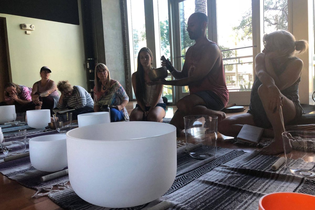 Hamid holding a brass Himalayan bowl in front of a seated group, frosted and clear crystal bowls on the floor between them