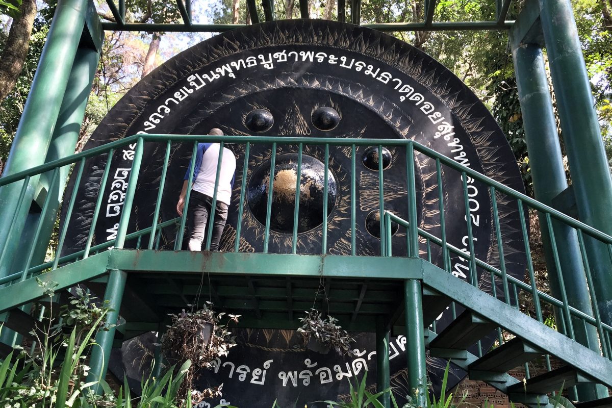 A large temple gong on a raised platform in Thailand, its face covered in Thai lettering