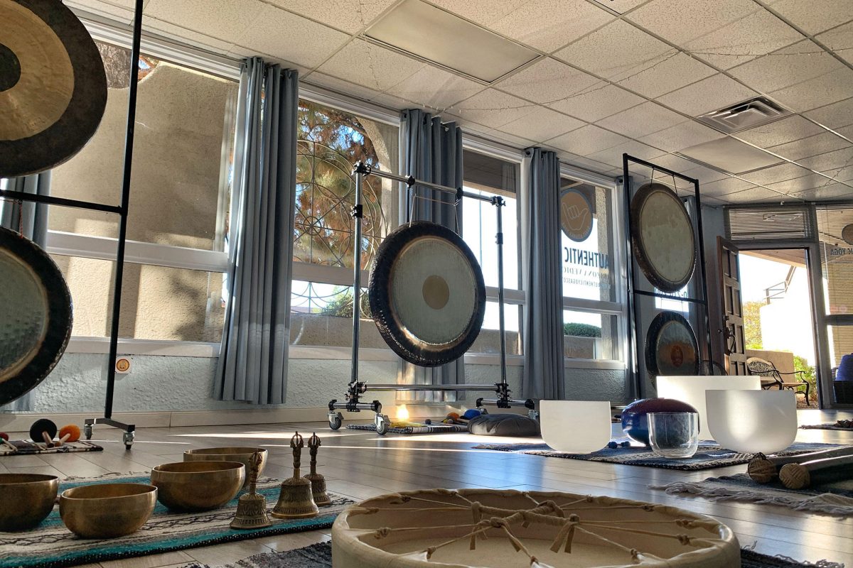 A studio laid out for a training, gongs on stands along a wall of windows, Himalayan bowls, crystal bowls, bells and a frame drum on rugs across the floor