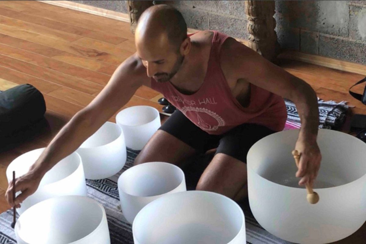 Hamid kneeling over a row of frosted crystal singing bowls with a mallet in each hand
