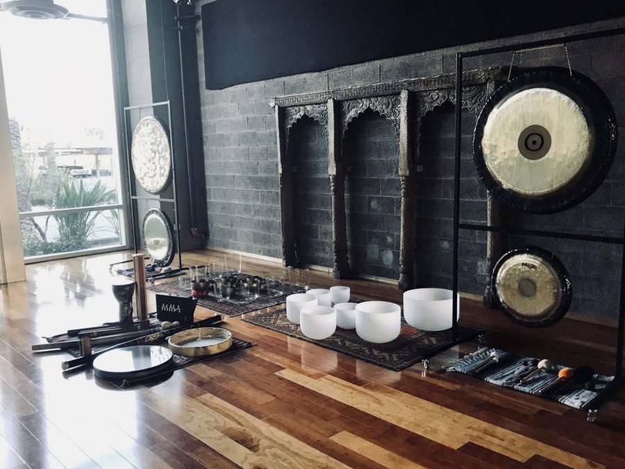 A studio floor with the whole set up laid out: two gongs hanging on stands, a row of crystal bowls, Himalayan bowls, a frame drum, didgeridoos and chimes on rugs