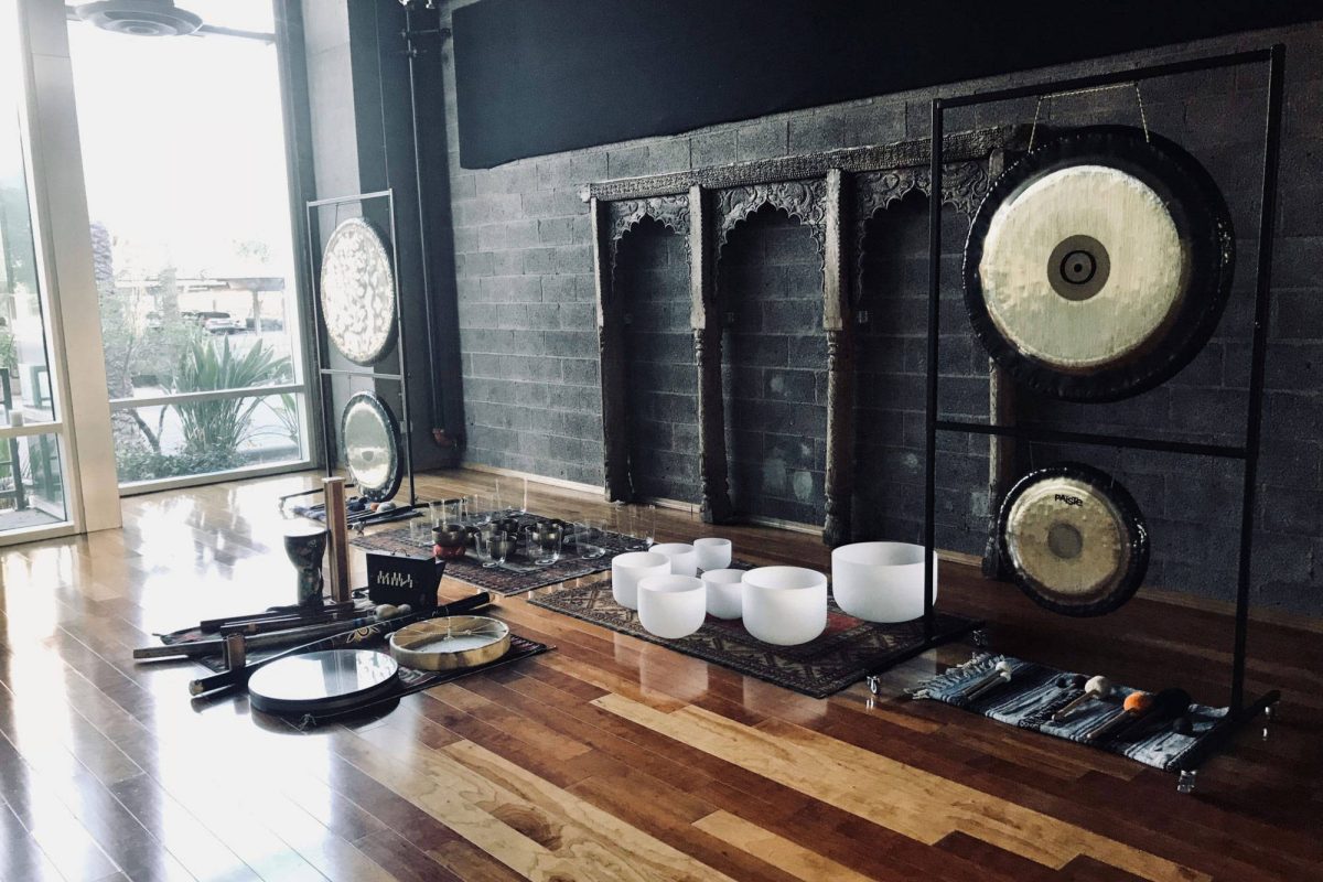 A studio floor with the whole set up laid out: two gongs hanging on stands, a row of crystal bowls, Himalayan bowls, a frame drum, didgeridoos and chimes on rugs