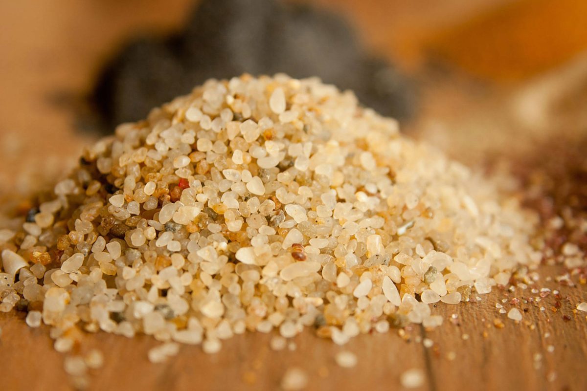 A small heap of pale silica sand grains on a wooden surface, photographed close enough to see individual grains