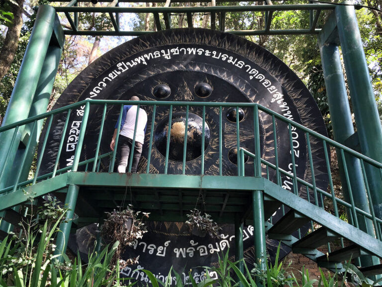 A large temple gong on a raised platform in Thailand, its face covered in Thai lettering