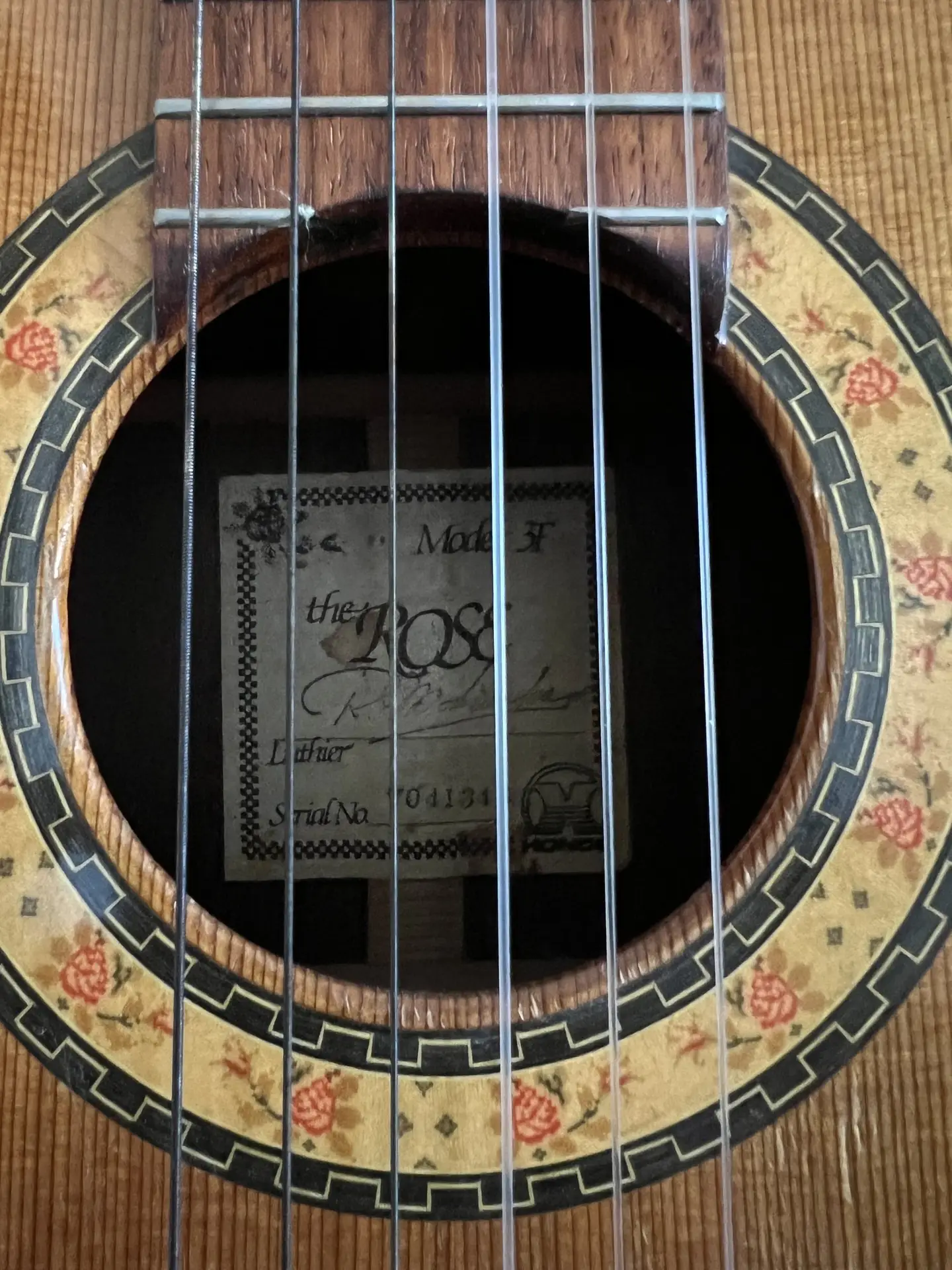 The soundhole of a classical guitar, its rosette painted with red roses, and inside a paper label reading the Rose, signed R. Matsuoka on the luthier line, with a Hondo logo in the corner